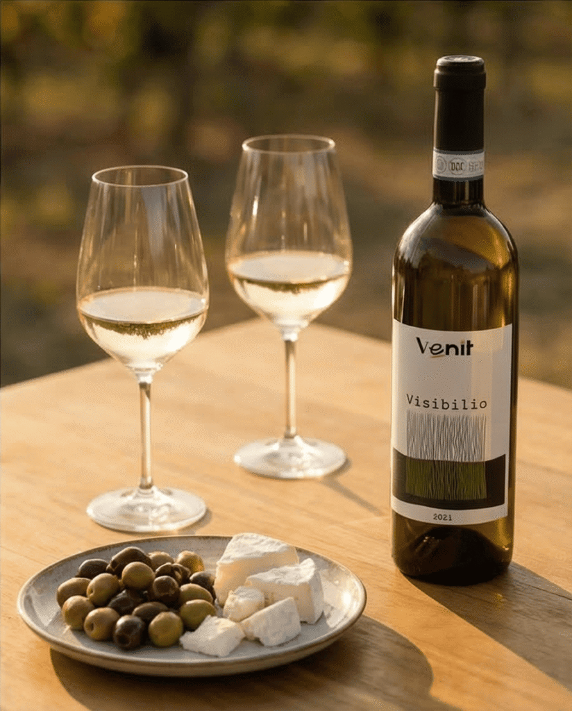 schaaltje olijven en kaas met fles Visibilio en twee glazen op houten tafel.