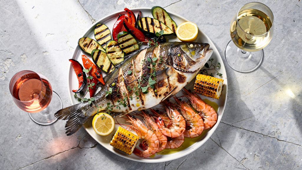 Gegrilde vis en groenten op een bord met glazen witte wijn en rosé. Gegrilde vis en groenten met witte wijn en rosé.